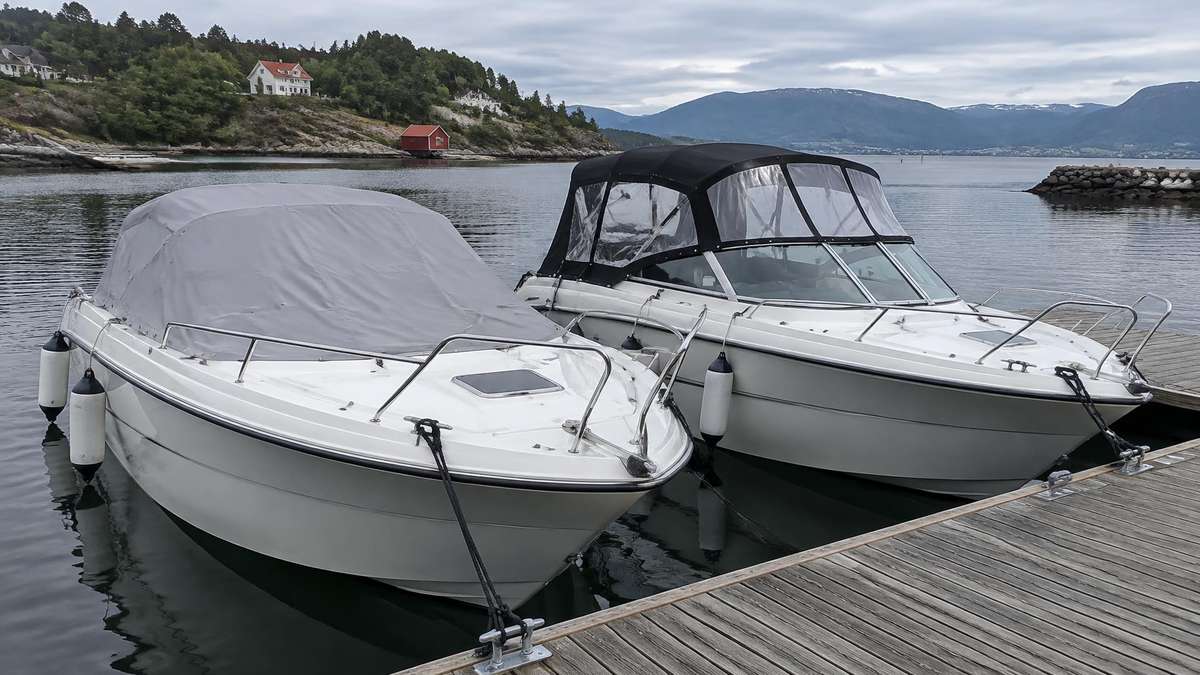 To motorbåter ved brygge, den ene med grå havnekalesje over cockpiten og den andre med full svart kalesje på bøyler