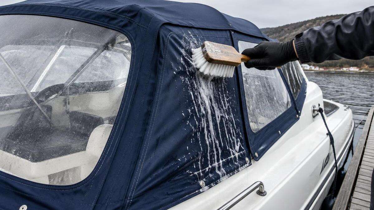 Hånd med hanske vasker en marineblå kalesje med myk børste og såpevann